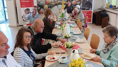 Menschen sitzen an einem langen Tisch beim Kaffeetrinken.