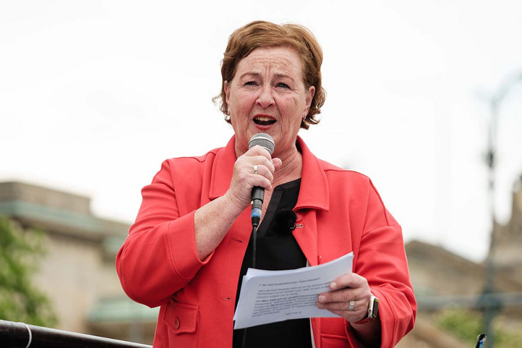 Frau steht auf der Ladefläche eines LKW und spricht in ein Mikrofon. 