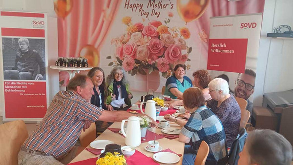 Frauen und Männer an geschmückter Kaffeetafel.