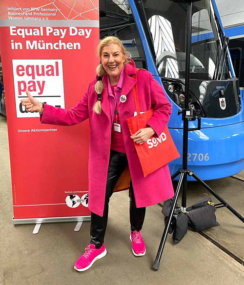 Frau steht neben einem Aussteller mit der Aufschrift "Equal Pay Day in München"
