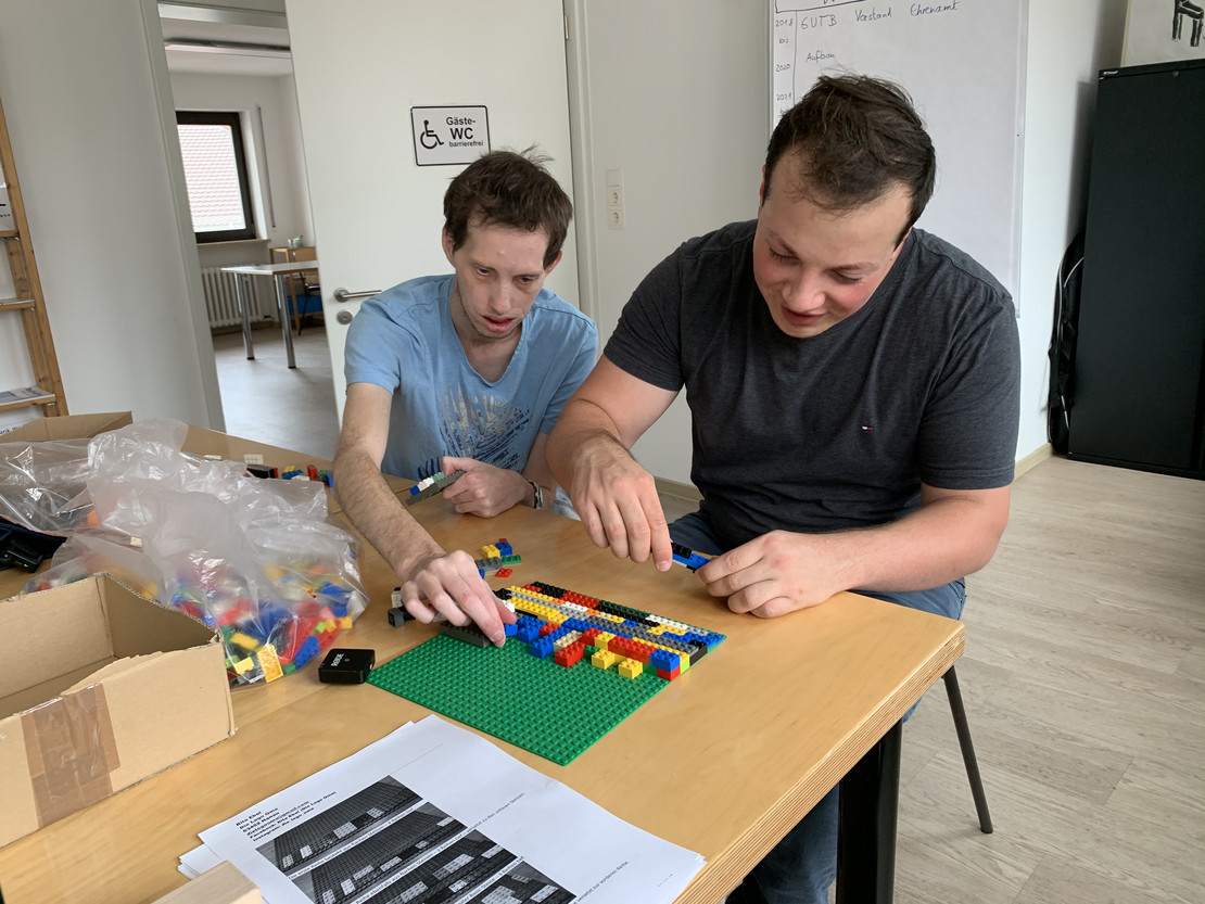 Zwei Männer bauen eine Rampe aus Legosteinen. 