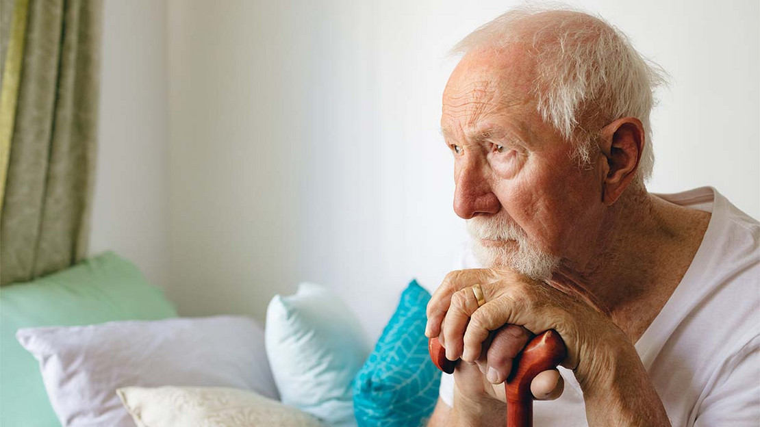 Älterer Mann stützt sich auf einen Stock und blickt nachdenklich.