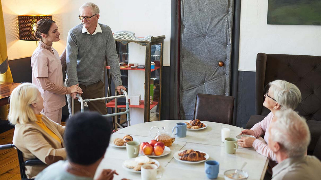 Eine Pflegekraft und mehrere ältere Menschen in einem Pflegeheim. 