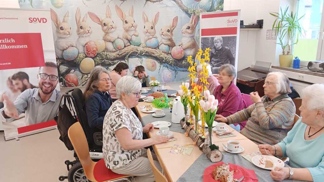 Frauen und Männer sitzen am Tisch, im Hintergrund ein Plakat mit Hasen.