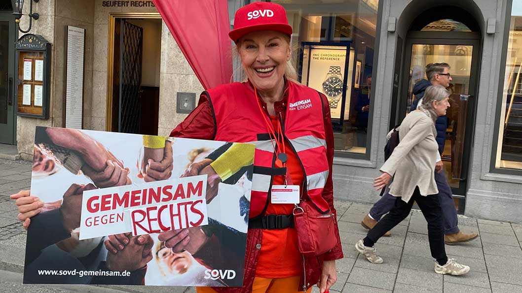 Frau mit roter Kleidung und SoVD-Schild. 