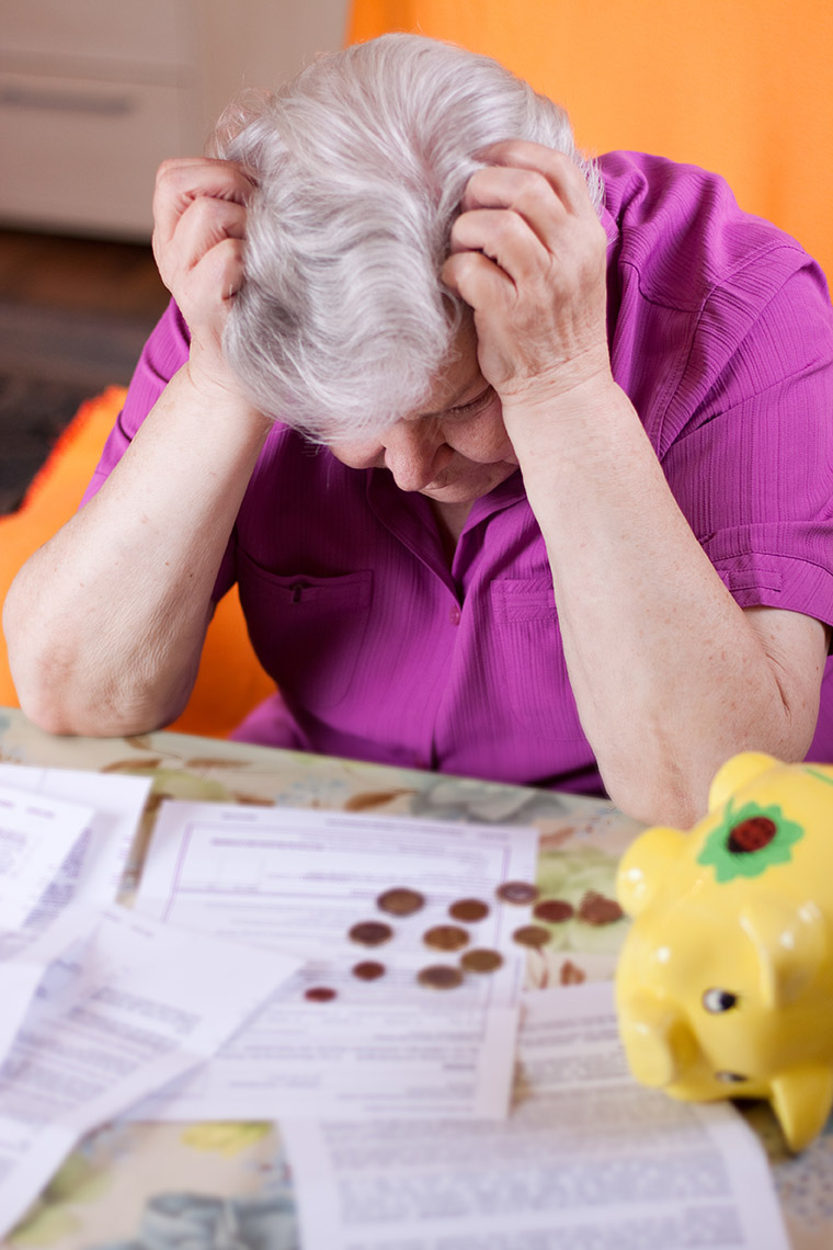 verzweifelte Seniorin schaut auf Rechnungen, -kleingeld und Sparschwein